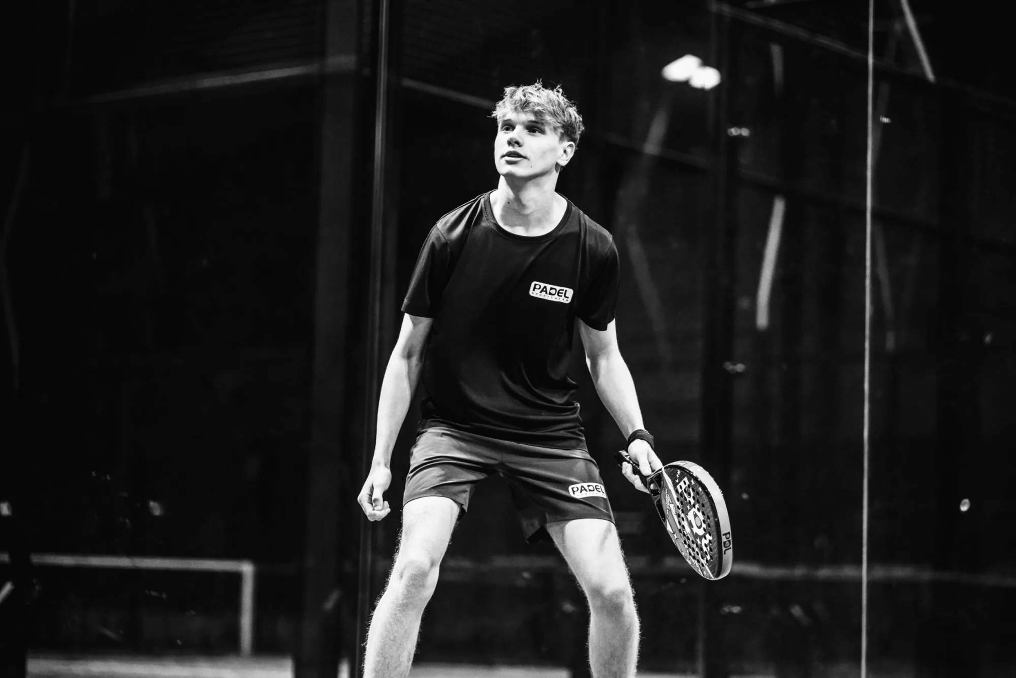 Padelspeler in een zwart Padel Sportswear-shirt op de padelbaan